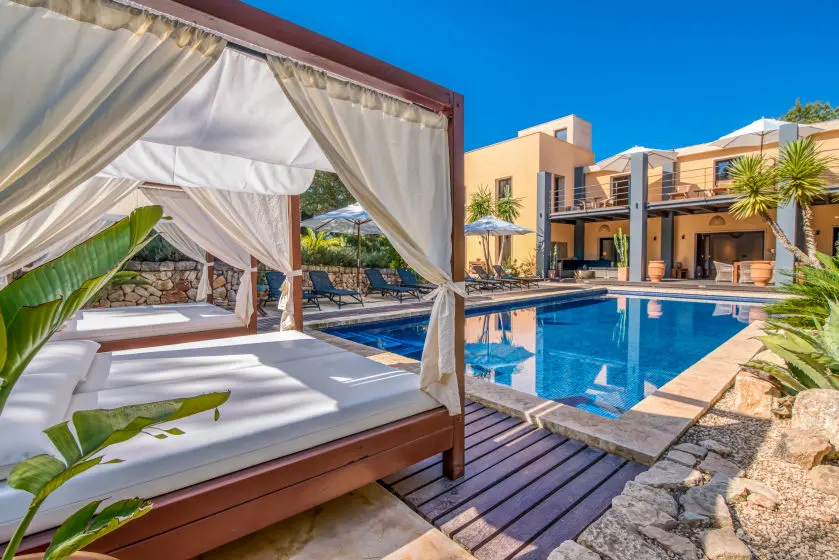 Himmelbett-Daybed mit Vorhängen am Pool, dahinter die Finca