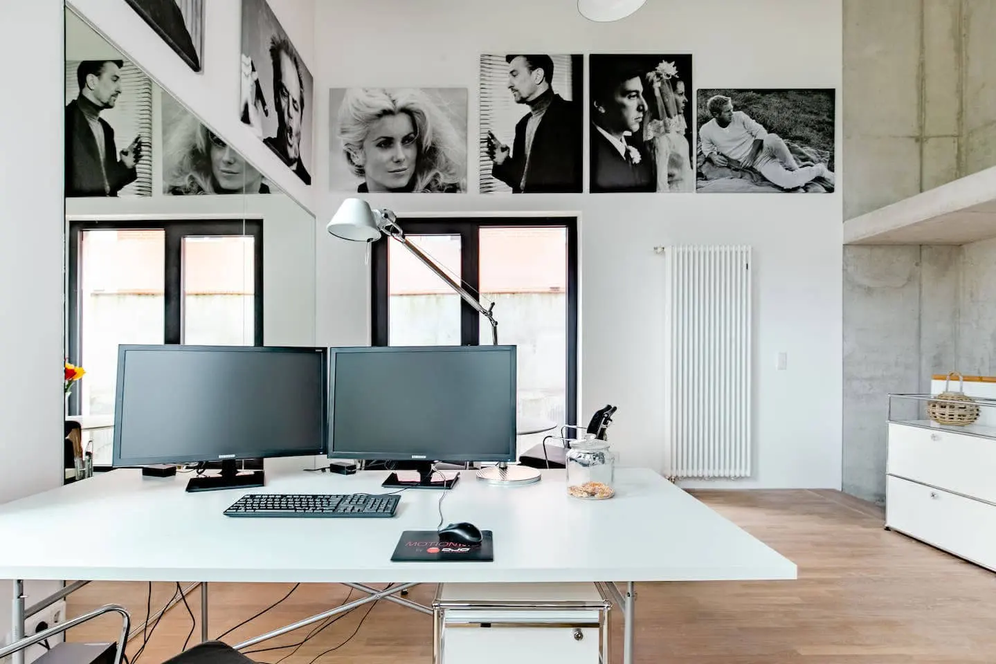 Weißer Schreibtisch mit zwei Monitoren vor Schwarz-Weiß-Porträts im Loft