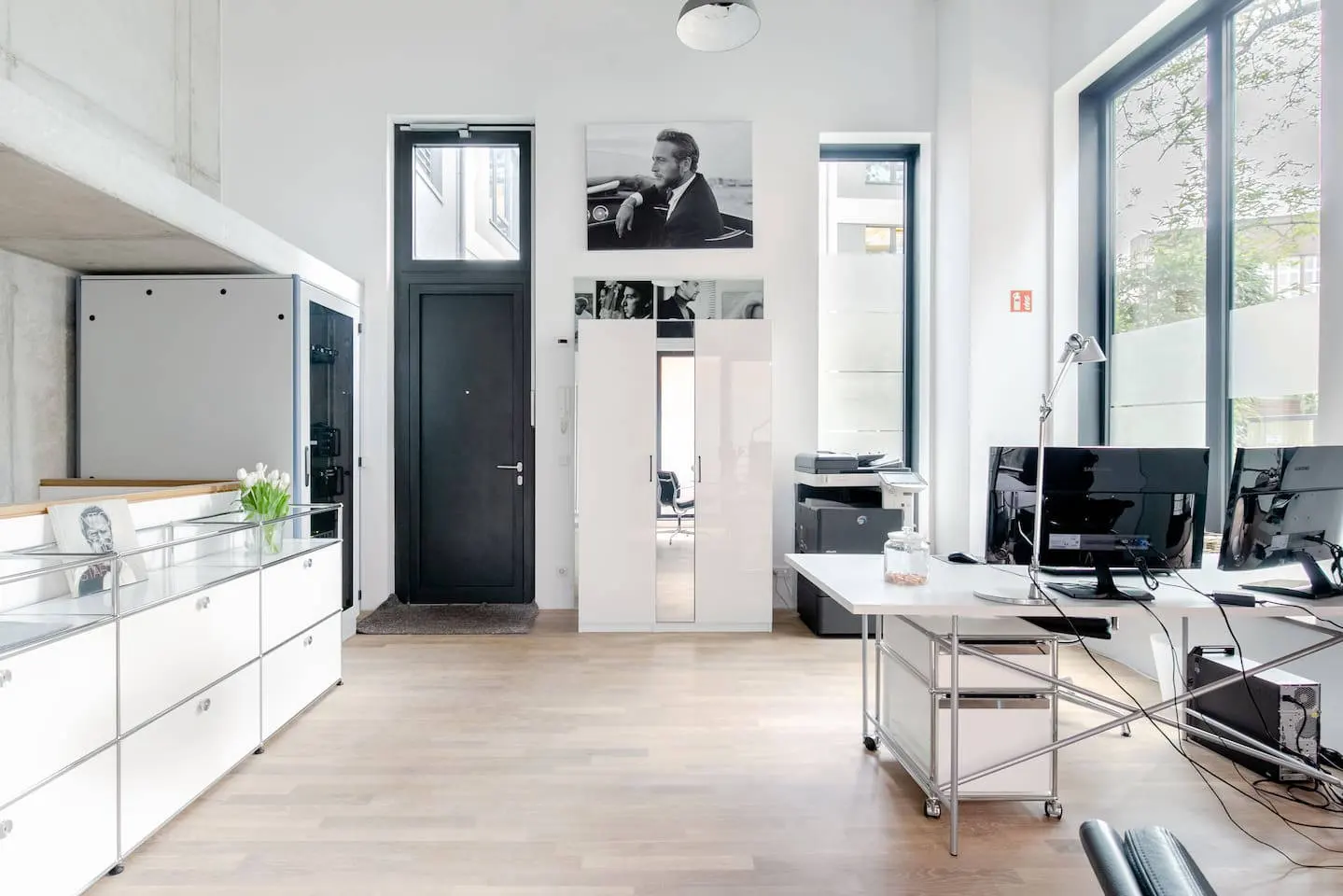 Loft mit Schreibtisch, USM-Sideboard und Eingangstür unter hohen Wänden