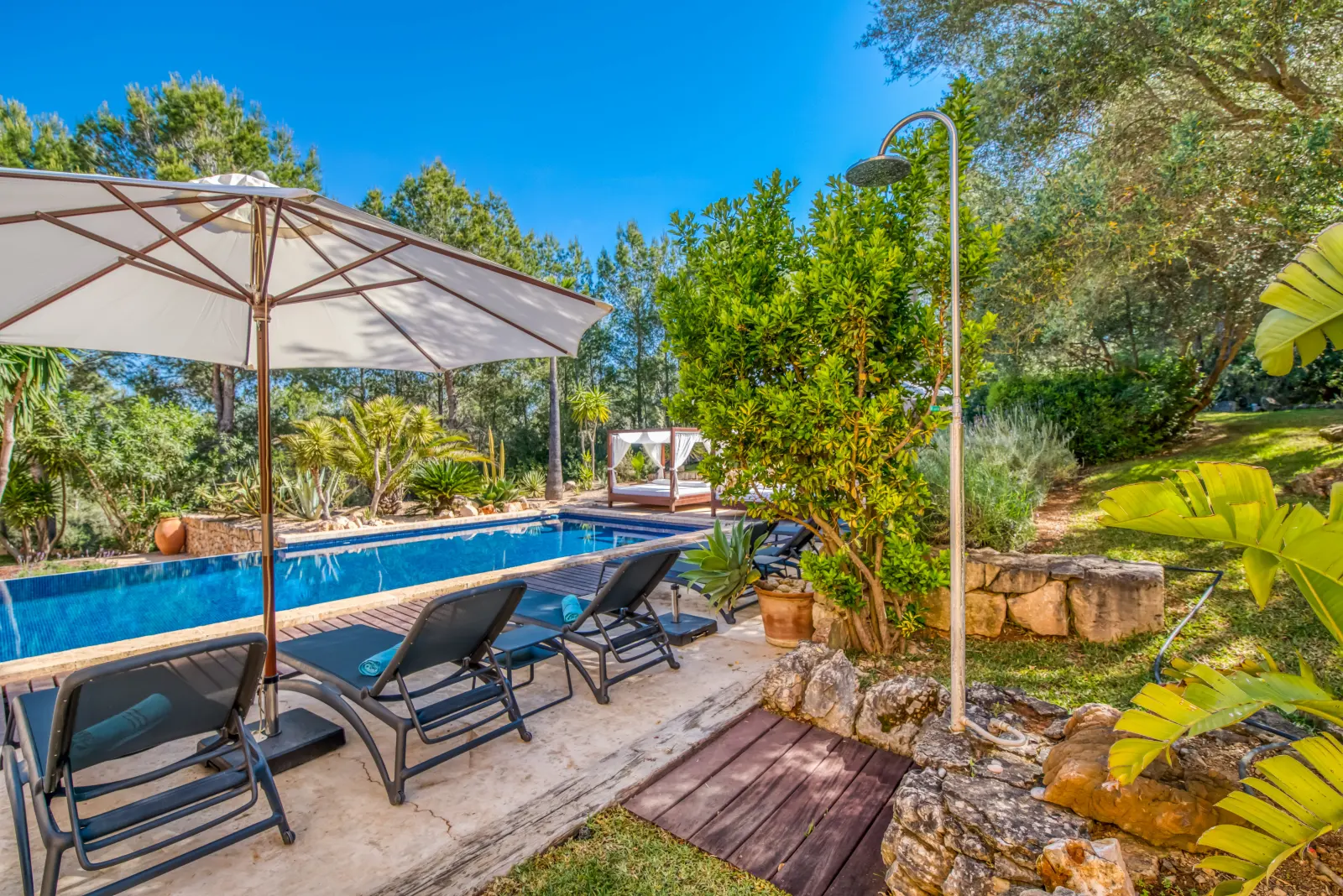 Poolterrasse mit Sonnenschirm, Liegen und Außendusche vor Mittelmeervegetation