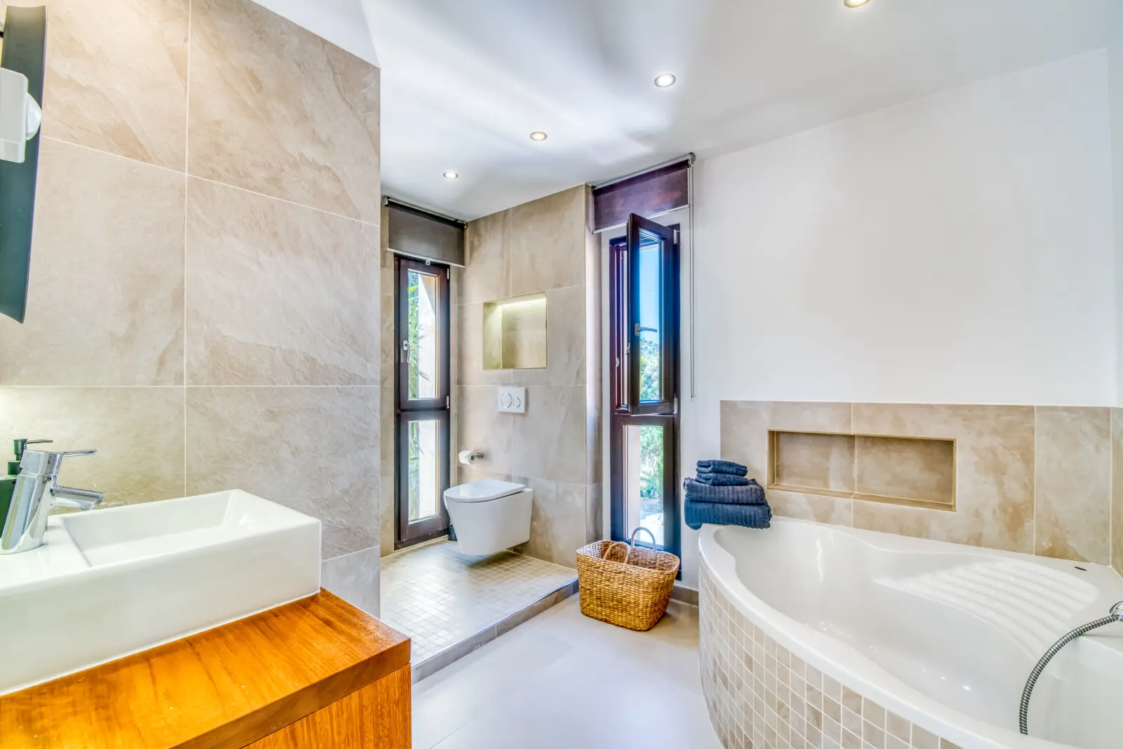 Bad mit Waschbecken, Eckbadewanne und Wand-WC in beigen Fliesen