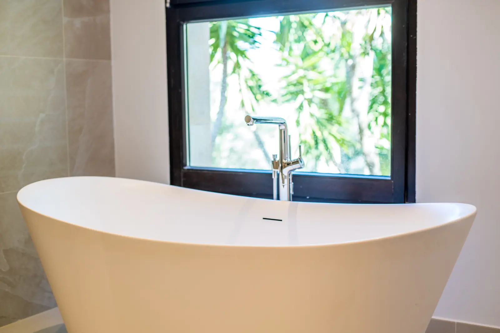 Freistehende weiße Badewanne unter einem Fenster mit Blick auf Blattwerk