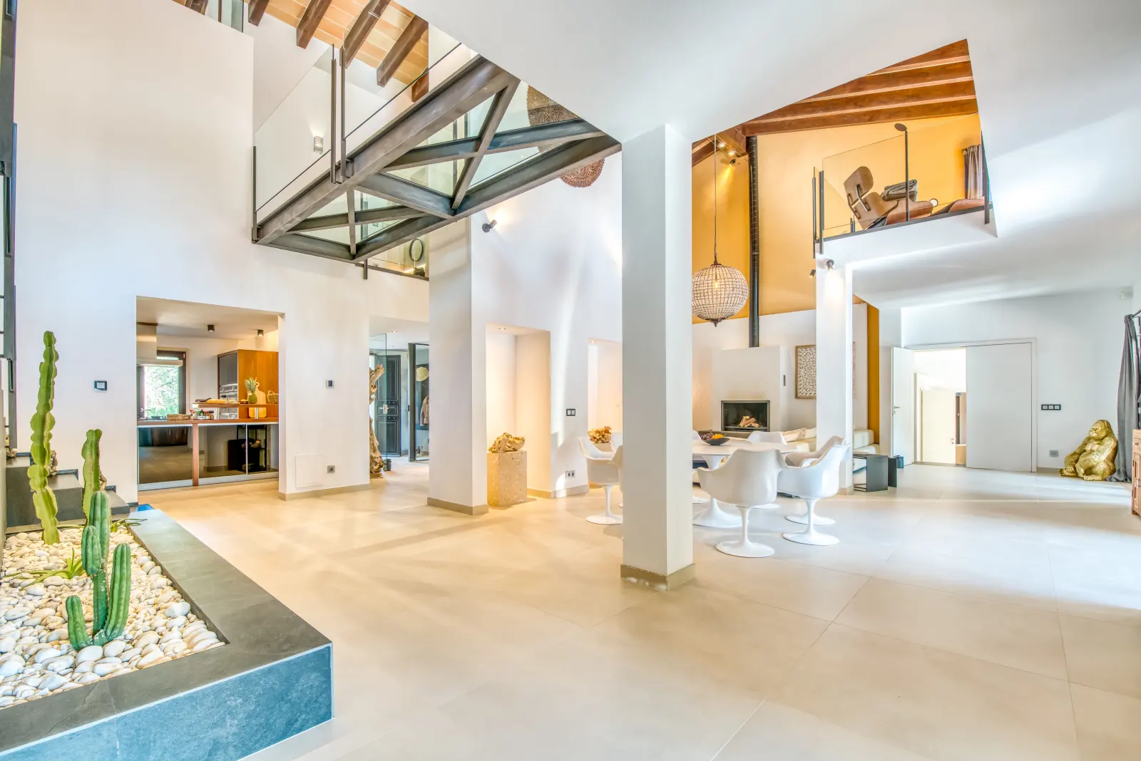 Hoher Wohnraum mit Galerie, Säulen, Kaktus-Pflanzbeet und Esstisch im Hintergrund