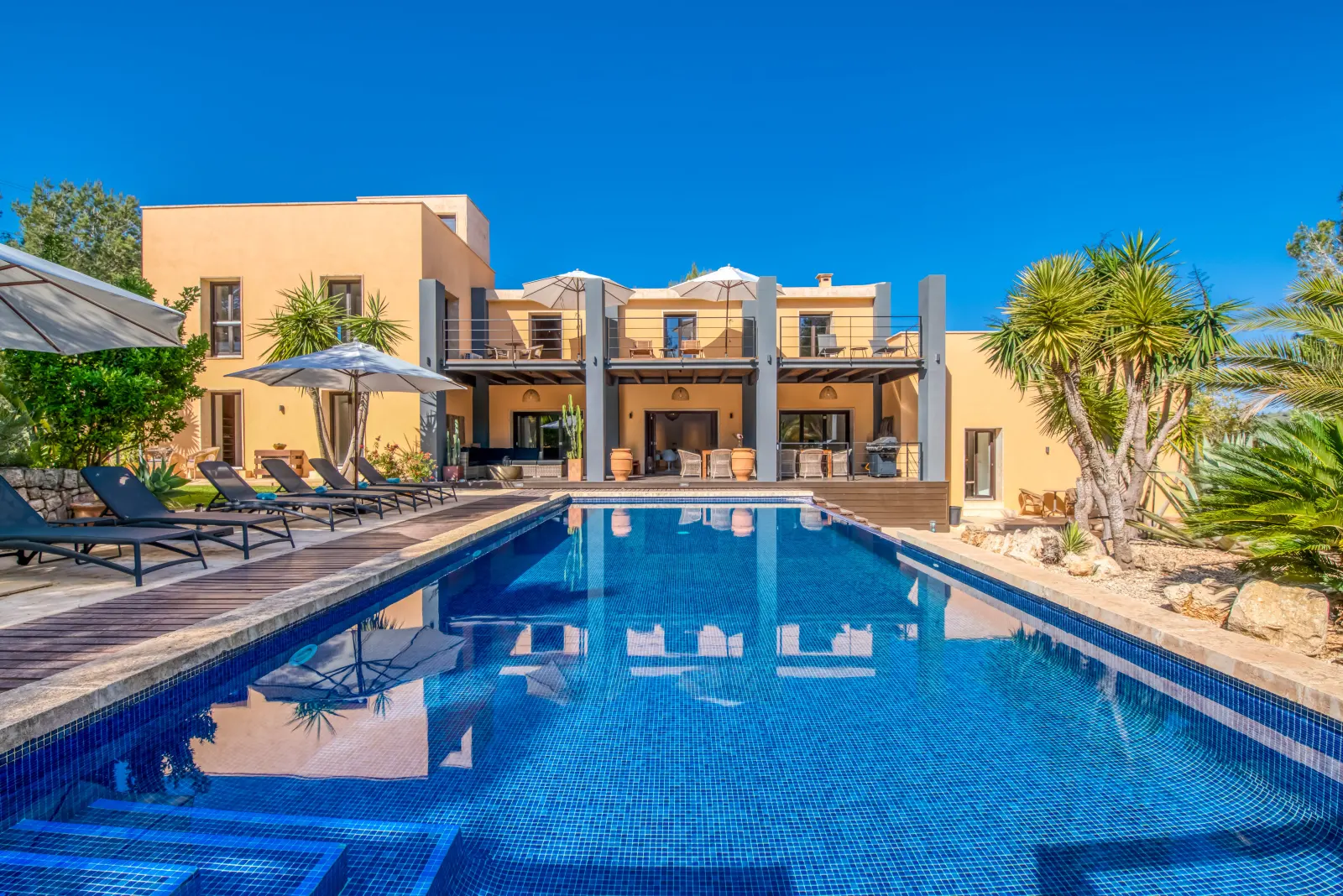 Pool mit Daybeds und Liegen, dahinter die zweistöckige Finca
