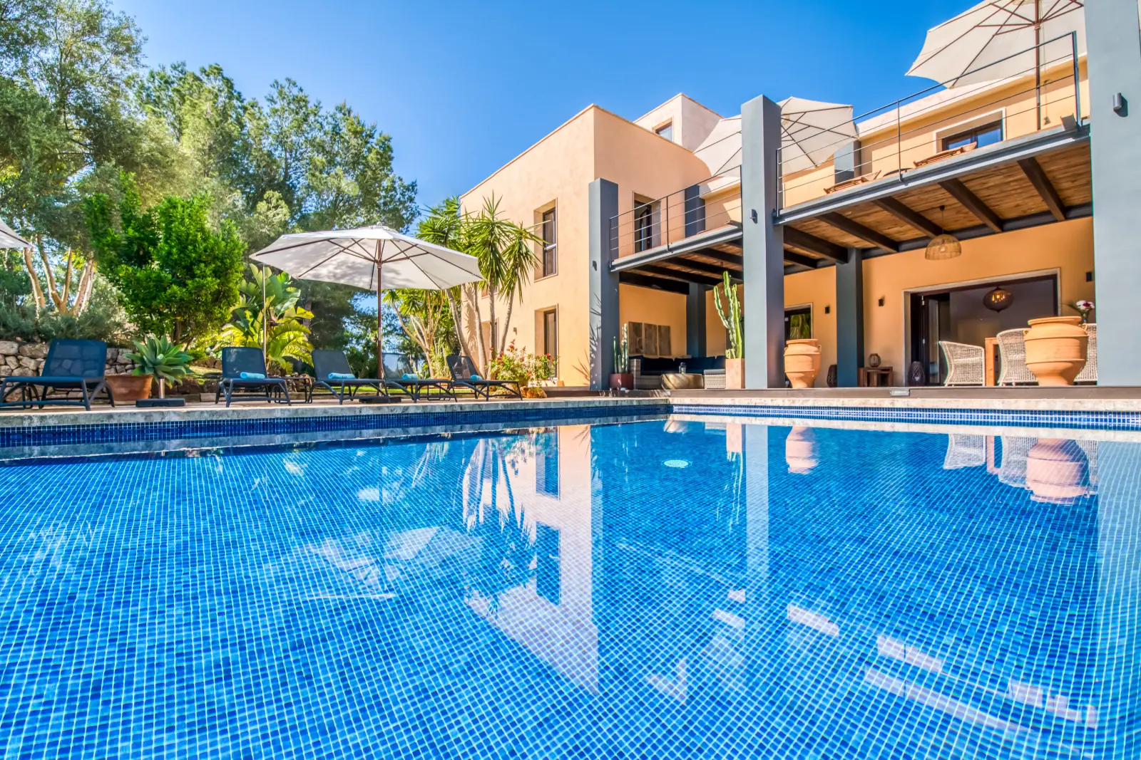 Poolrand mit Sonnenschirmen und Liegen vor der Terrasse der Finca