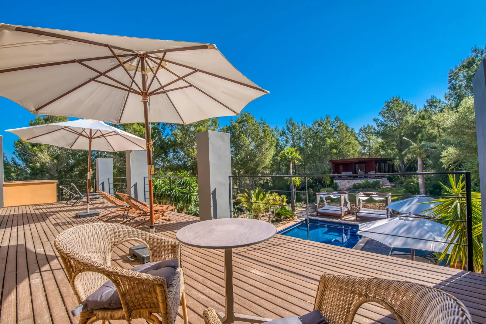 Obere Holzterrasse mit Rattansesseln, Tisch und Blick auf den Pool