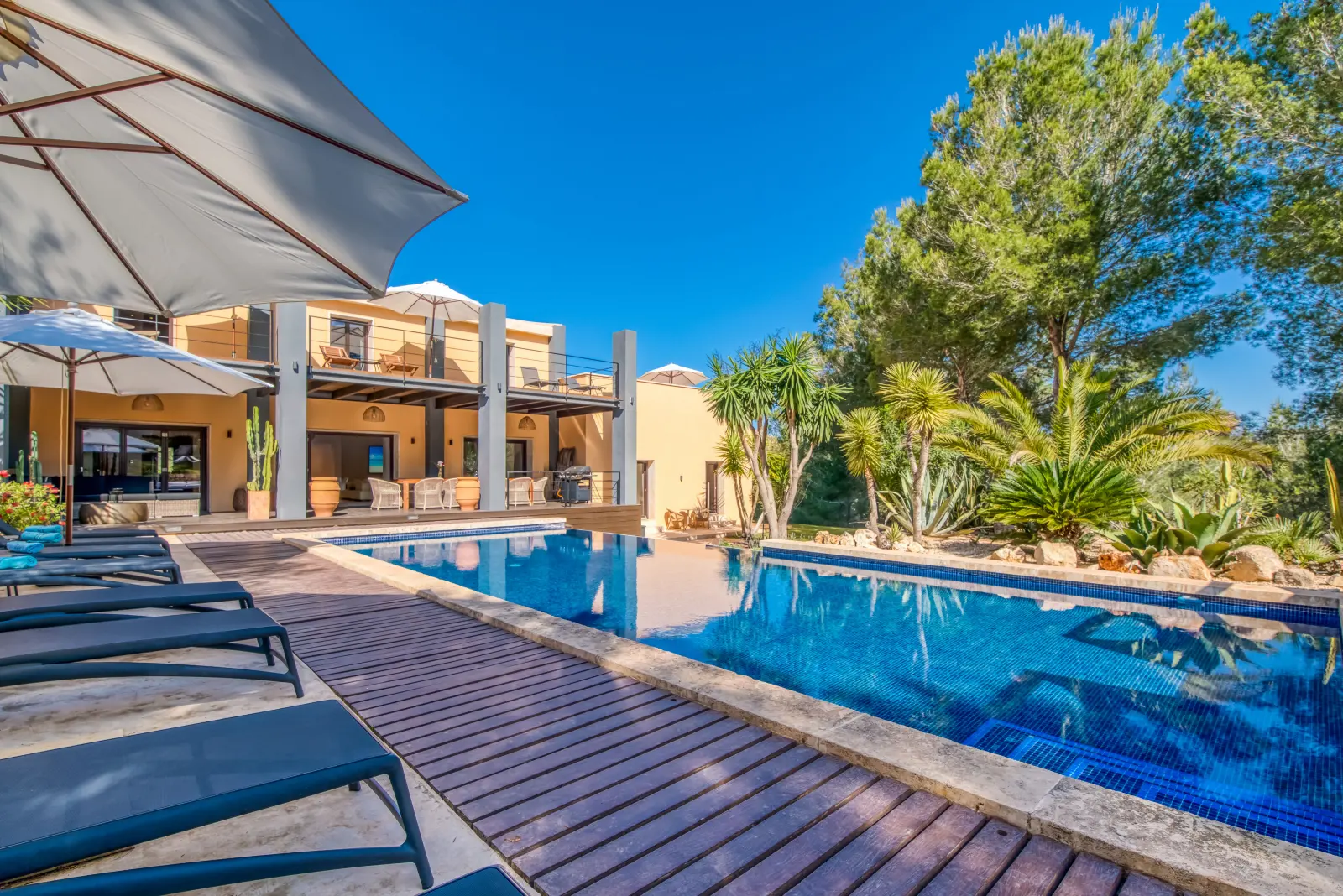 Holzsteg am Pool entlang mit Liegen, Sonnenschirm und Finca im Hintergrund