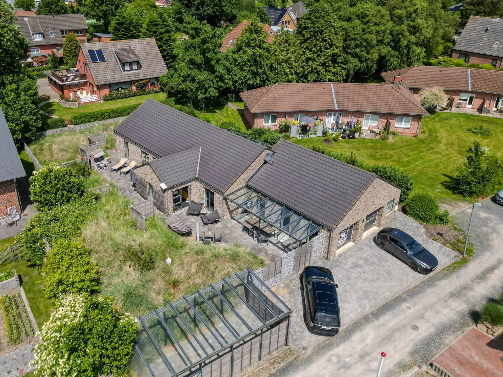 Luftbild des Klinkerhauses mit Glasanbau, Garten und Auto auf der Auffahrt
