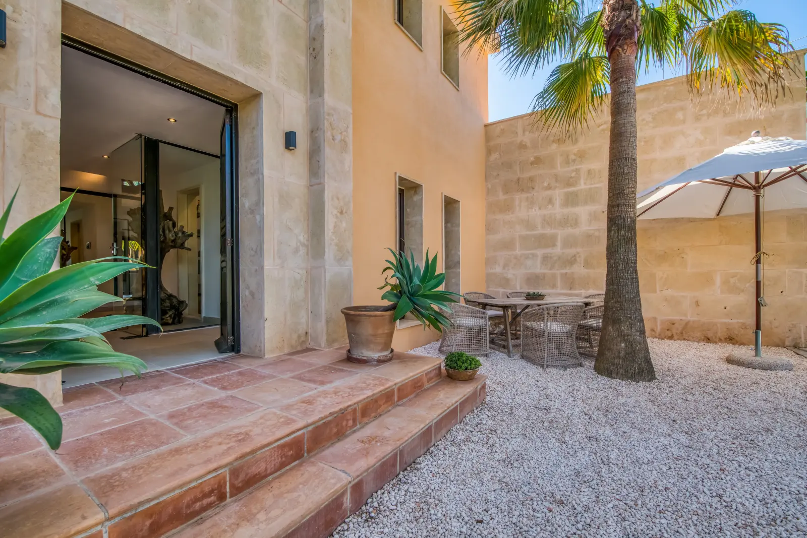 Eingangsbereich der Finca mit Terrakottastufen, Palme und Sitzgruppe im Kieshof
