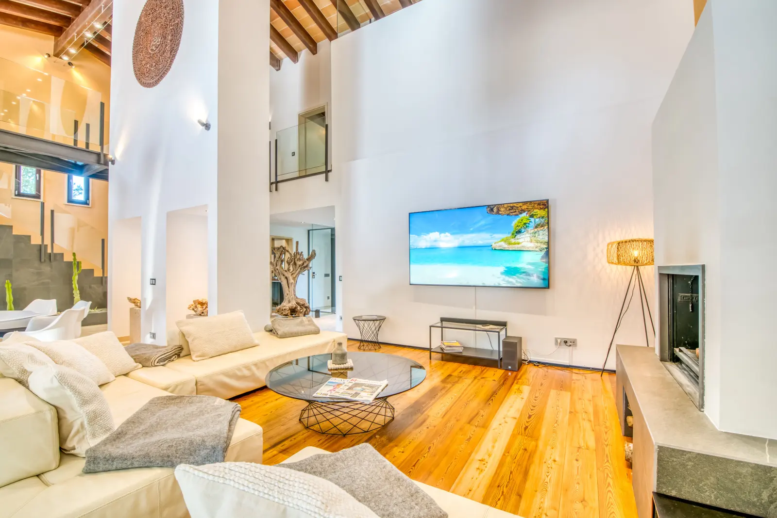 Wohnbereich mit weißem Sofa, Glastisch und großem Fernseher in der hohen Halle