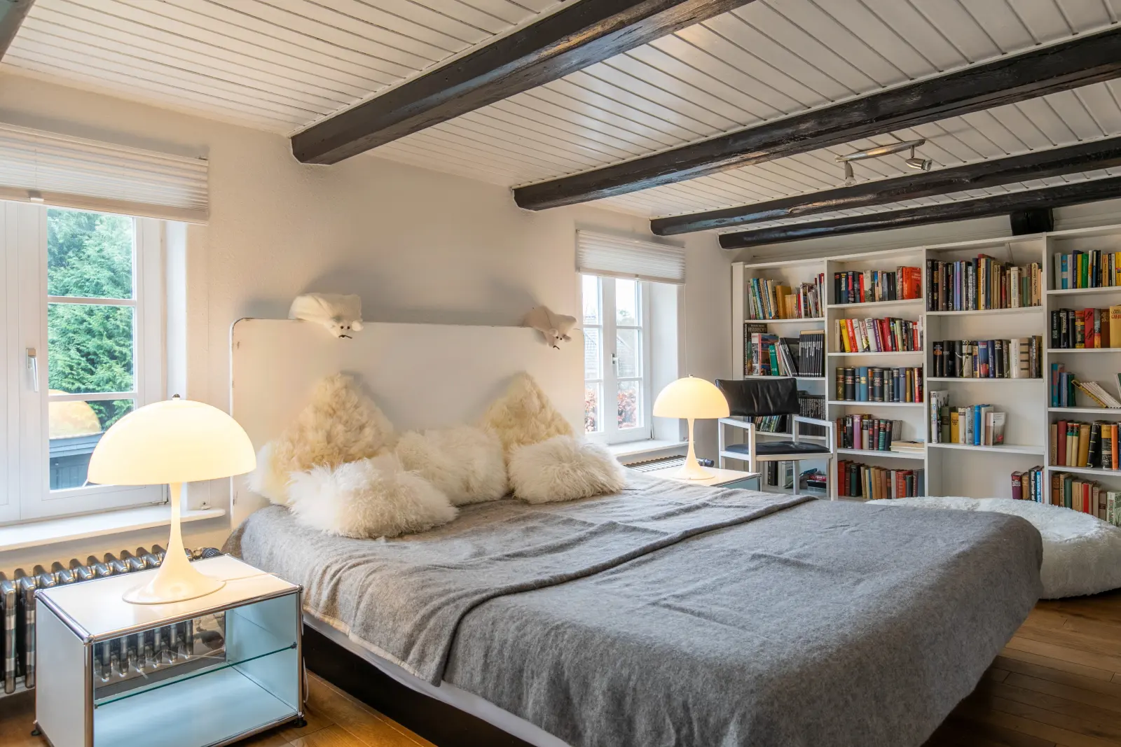 Schlafzimmer mit Doppelbett, Holzbalken, Bücherregal und Pilzlampen