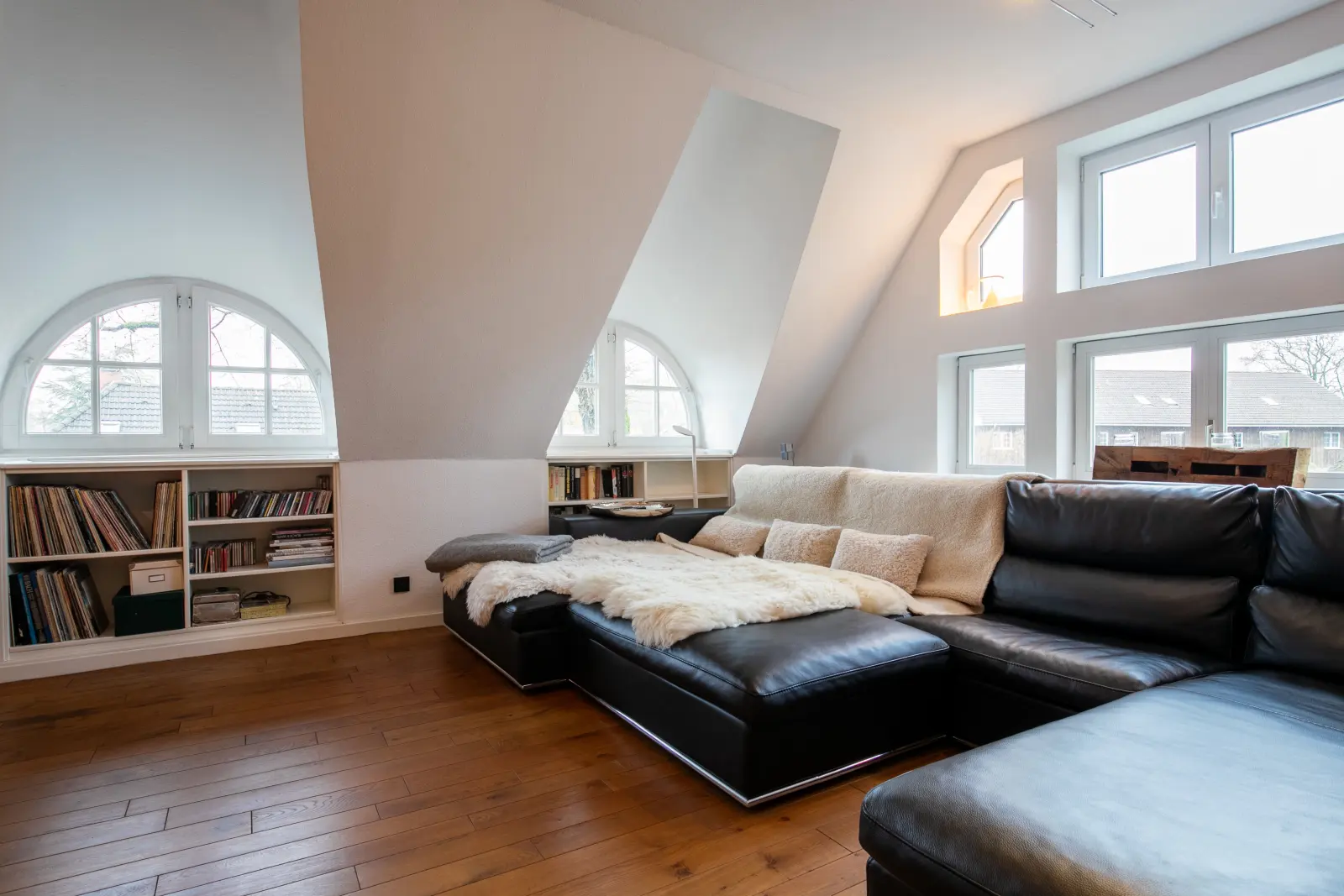 Wohnbereich unterm Dach mit schwarzem Ledersofa, Fellen und Bücherregalen