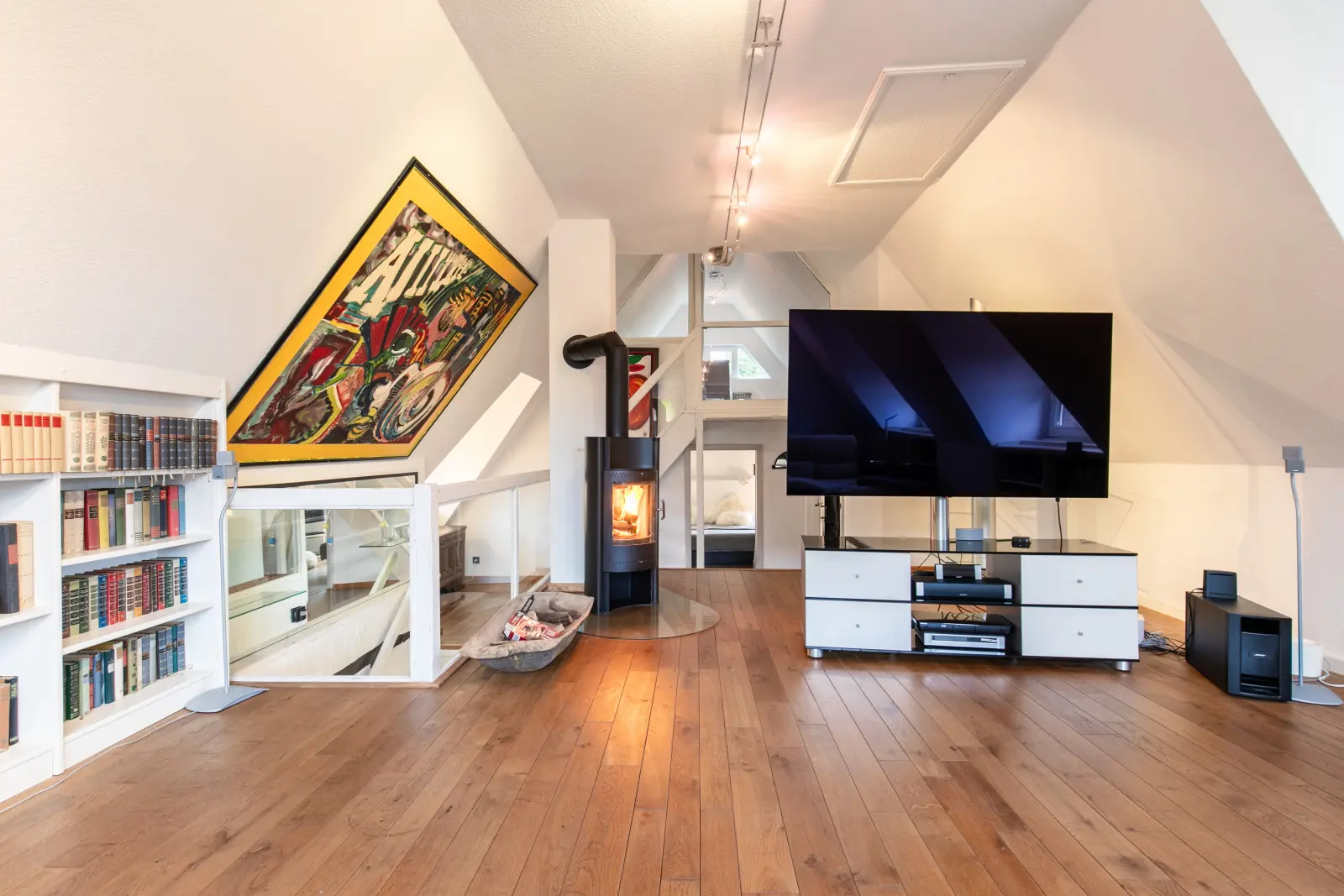 Dachgeschoss mit Kaminofen, Fernseher, Bücherwand und buntem Wandbild