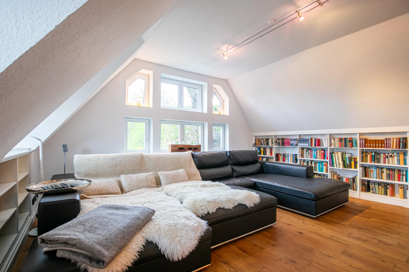 Wohnlandschaft mit Ledersofa und Fellen, Bücherregal unter der Dachschräge