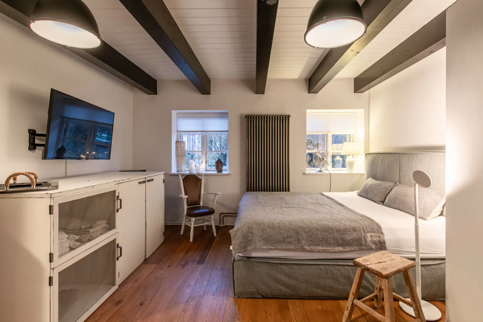 Schlafzimmer mit Wand-TV, Kommode, Doppelbett und Deckenbalken