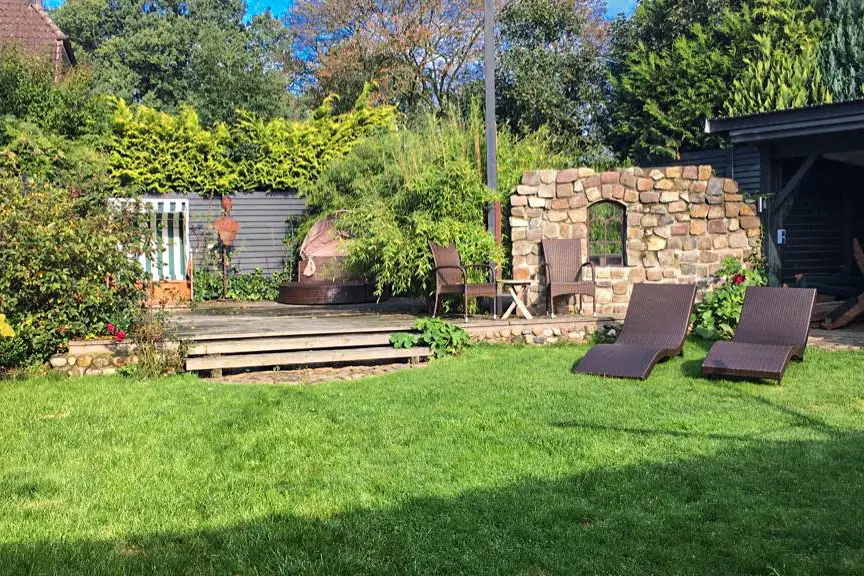 Garten mit Rasen, Sonnenliegen, Holzterrasse und Natursteinmauer