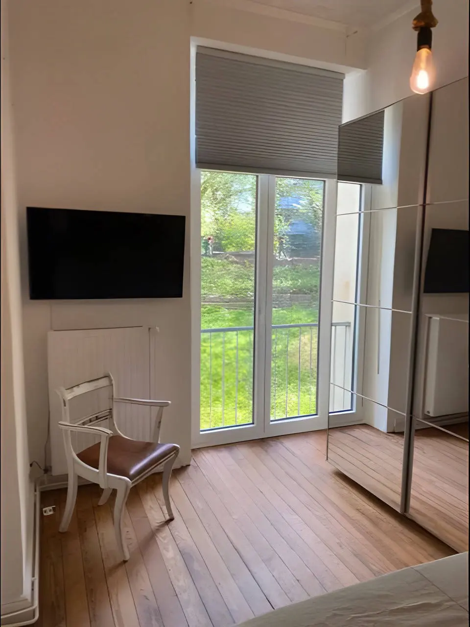Zimmer mit Balkontür, Wand-TV, Stuhl und Spiegelschrank