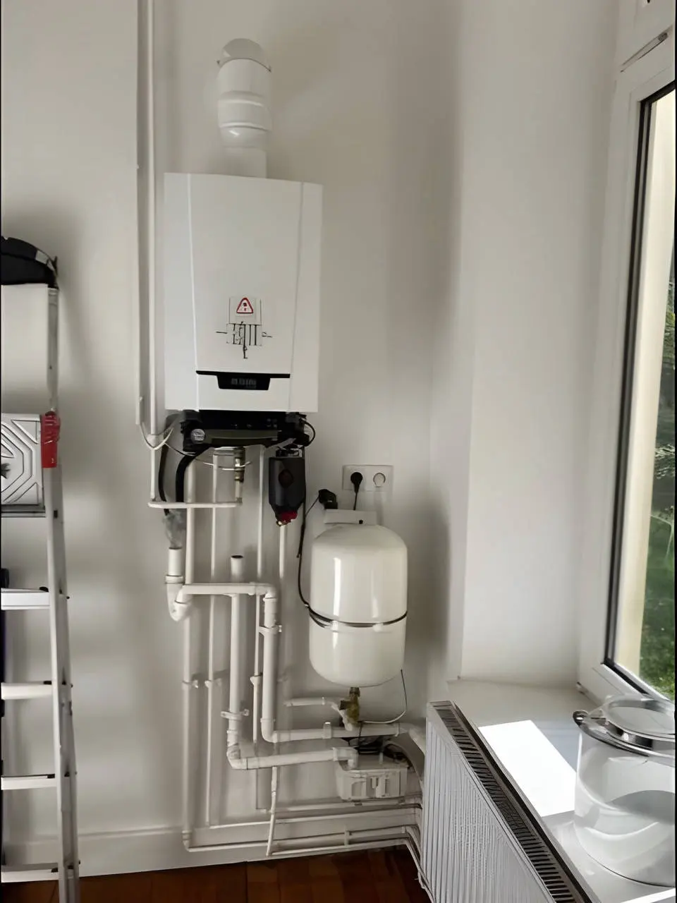 Gastherme mit Rohren und Ausdehnungsgefäß neben dem Fenster