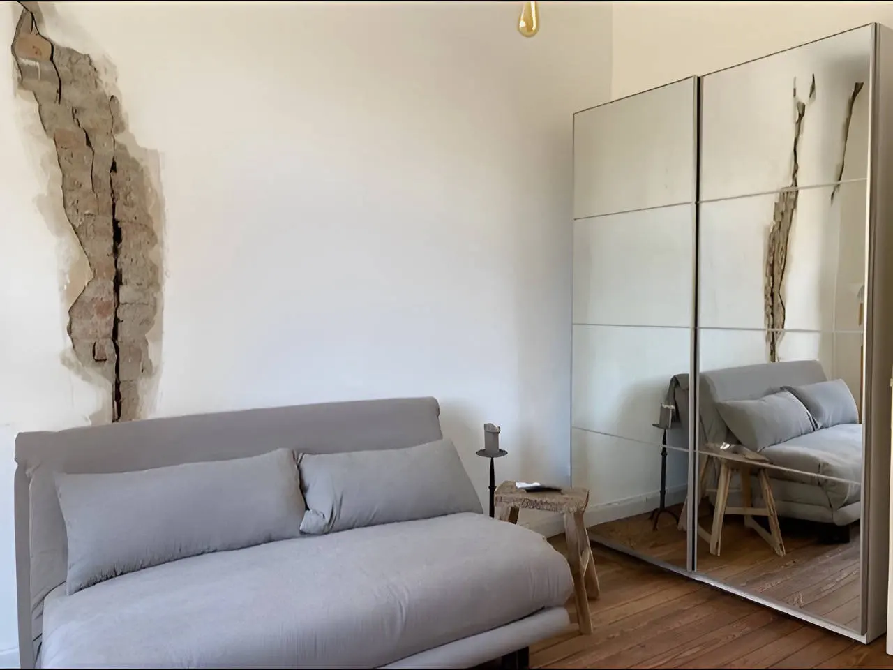 Schlafsofa neben verspiegeltem Kleiderschrank, an der Wand abgeplatzter Putz