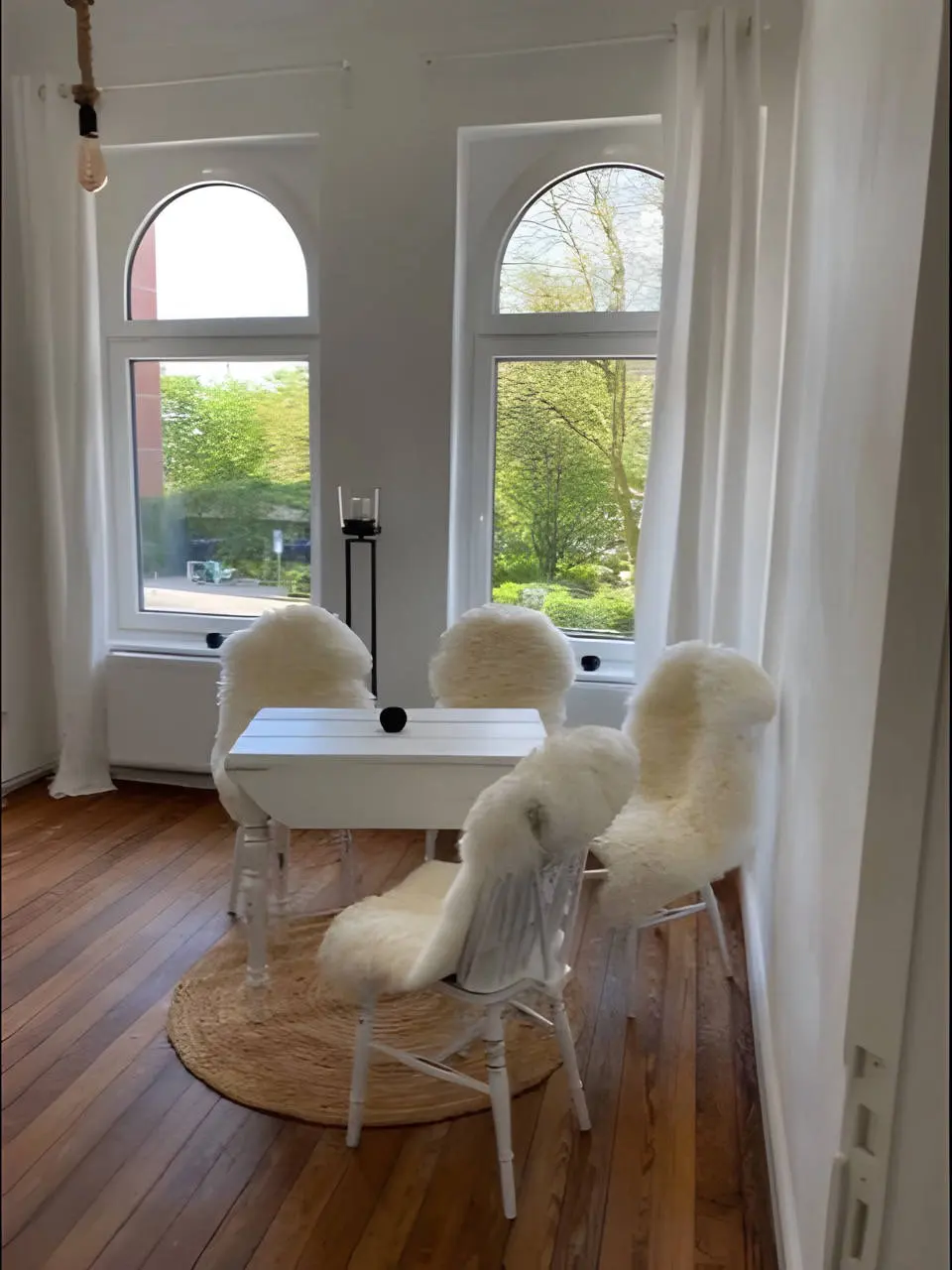 Esstisch aus weißem Holz mit Schaffellstühlen vor zwei Bogenfenstern
