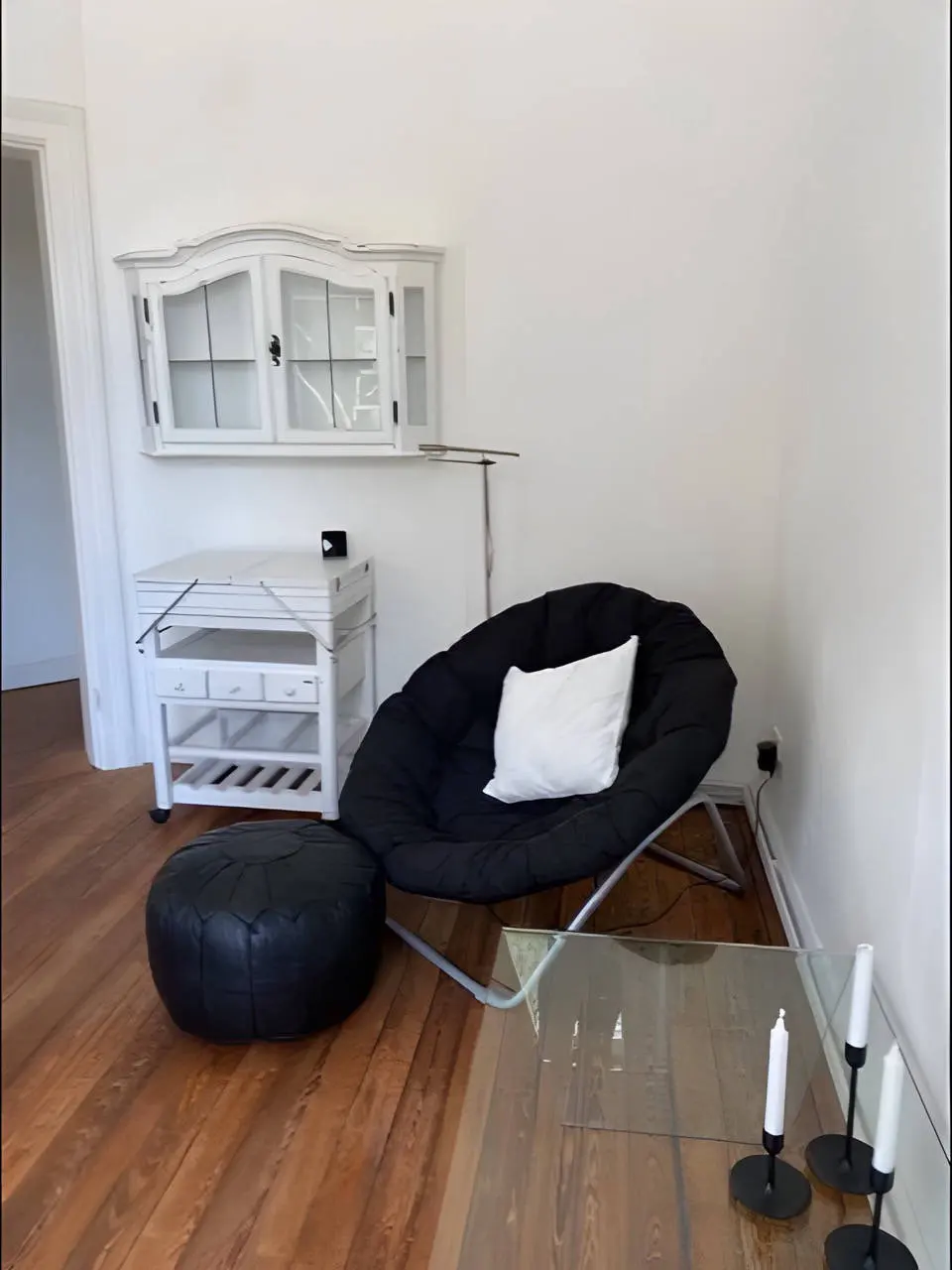 Schwarzer Sessel mit weißem Kissen, weißer Rollwagen und Wandschrank im Wohnzimmer