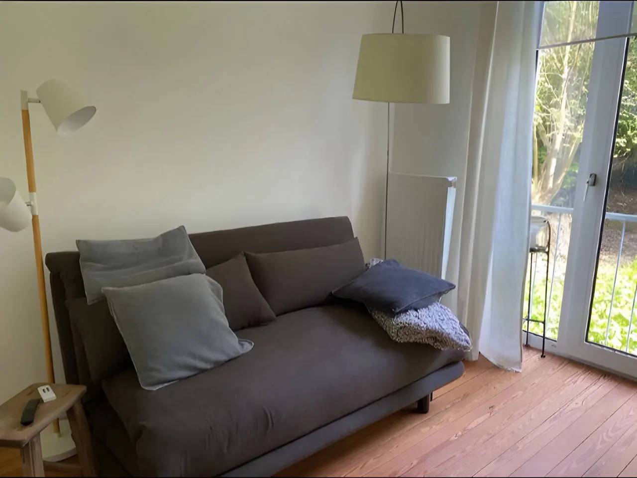 Schlafsofa in Dunkelgrau mit Kissen und Balkontür, daneben Stehlampe