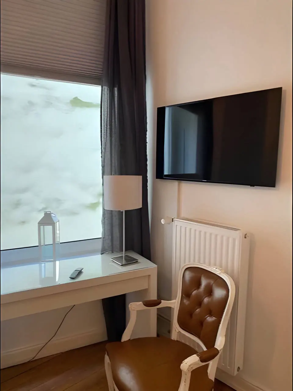 Arbeitsplatz mit Schreibtisch, Polsterstuhl, Wand-TV und Heizkörper am Fenster