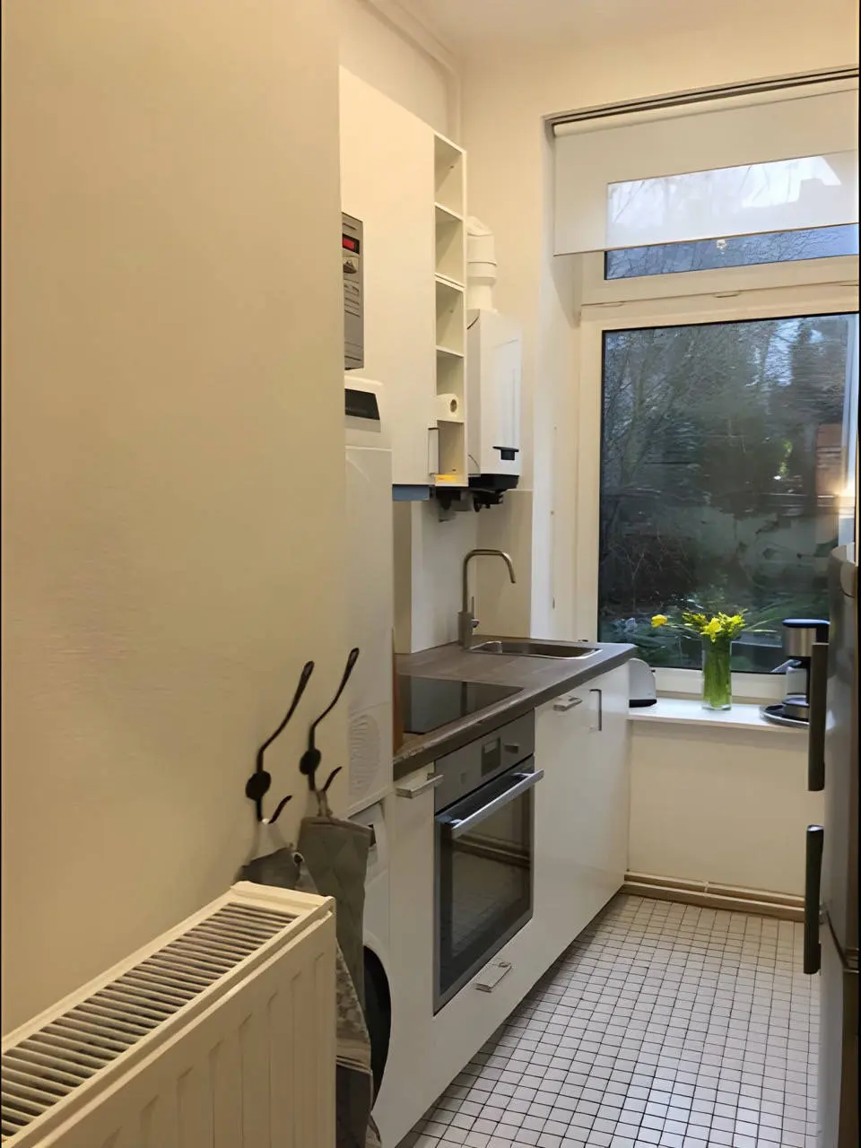 Schmale Küche mit Fenster zum Garten, Backofen und weißem Fliesenboden