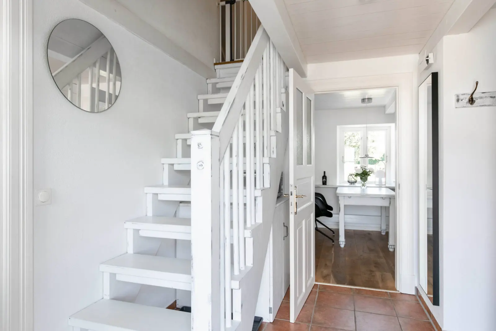 Flur mit weißer Treppe, Rundspiegel und Terrakottaboden