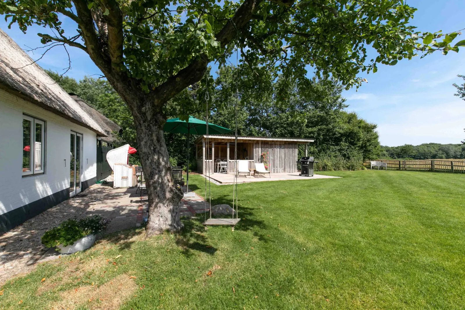 Gartenseite der Kate mit großem Baum, Schaukel und überdachtem Holzpavillon