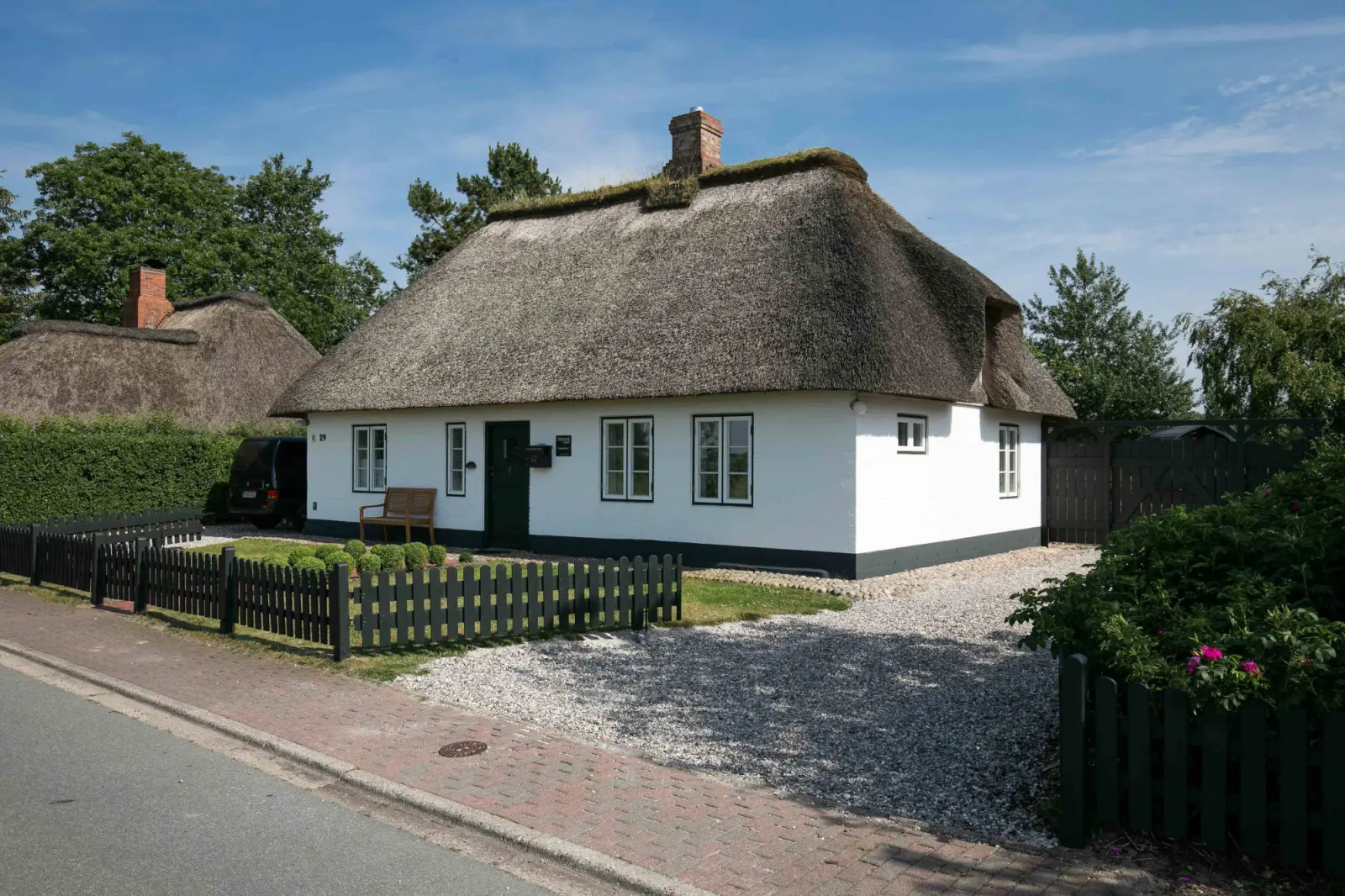 Reetdachkate von der Straßenseite mit Kiesauffahrt und Gartenzaun