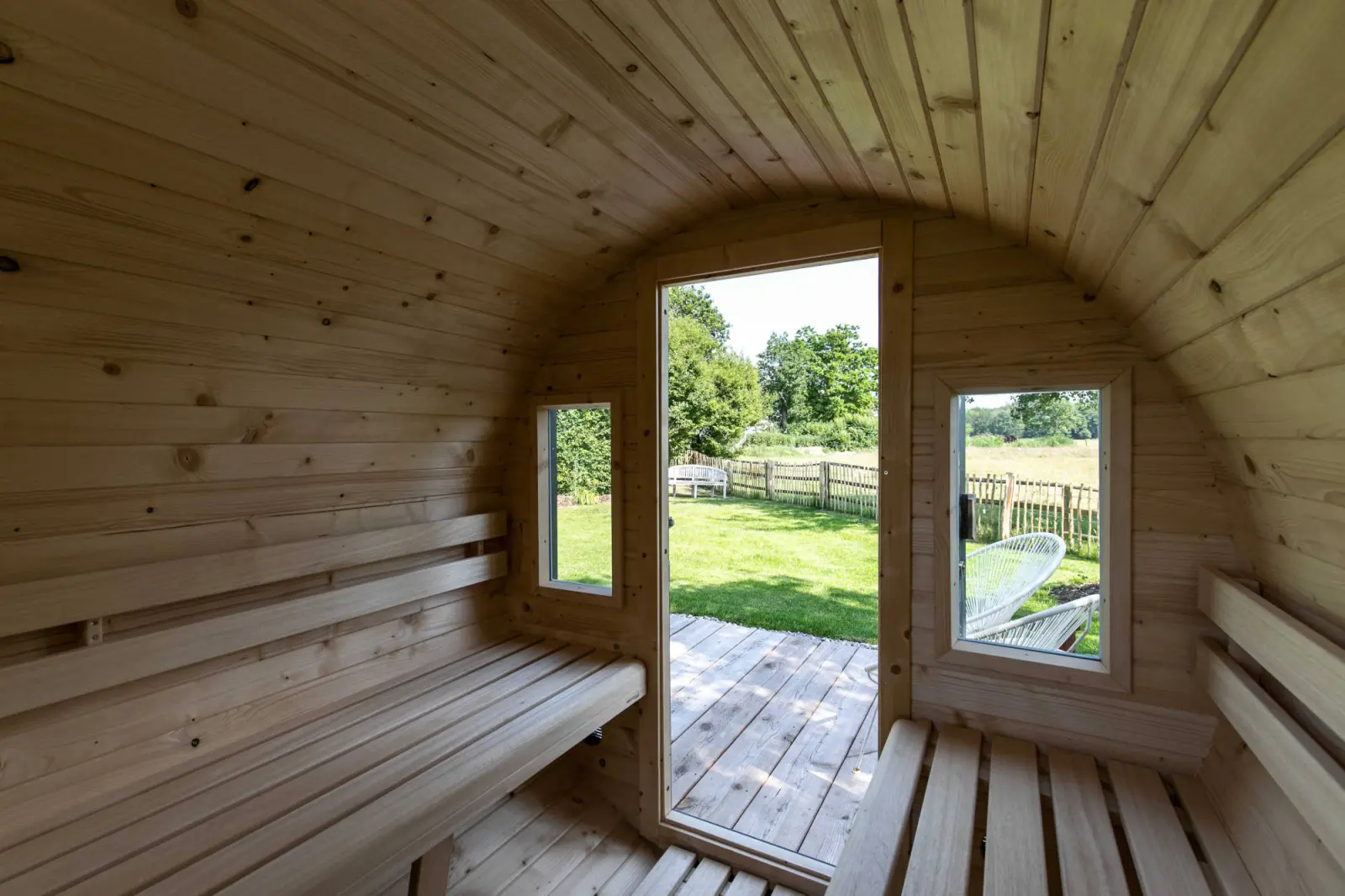 Innenraum der Fasssauna mit Holzbänken, offener Tür und Gartenblick
