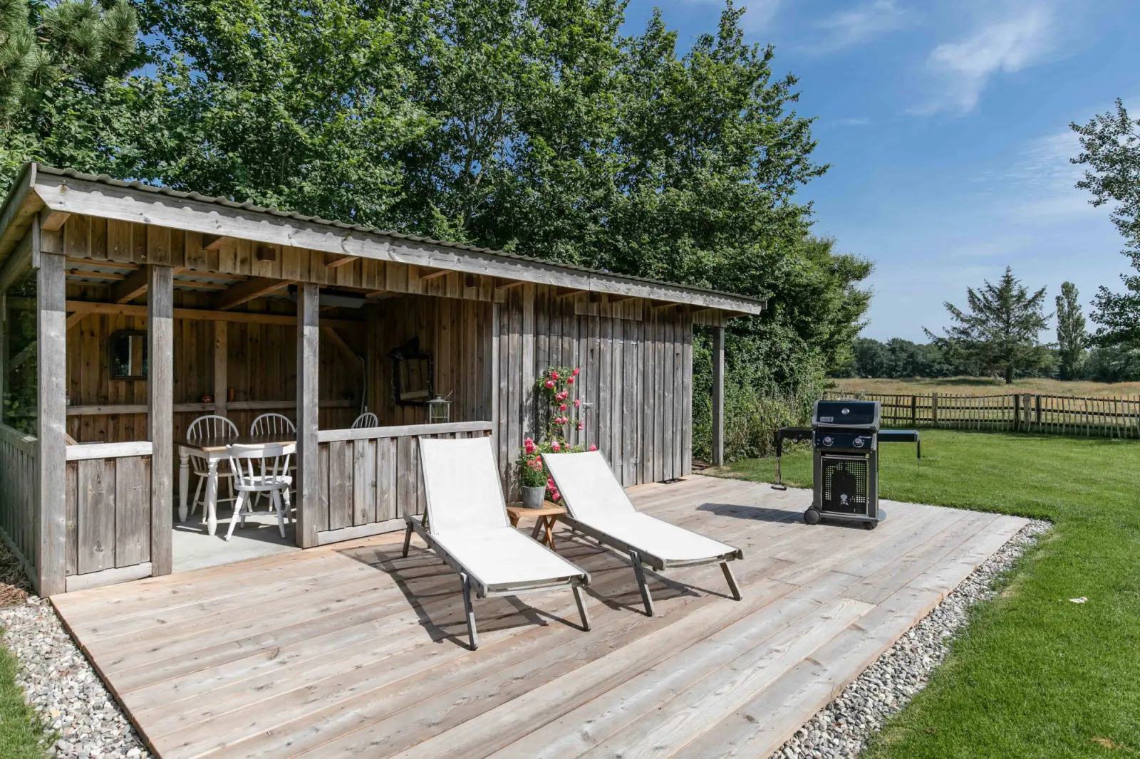 Pavillon mit zwei Sonnenliegen auf Holzdeck und Grill im Garten