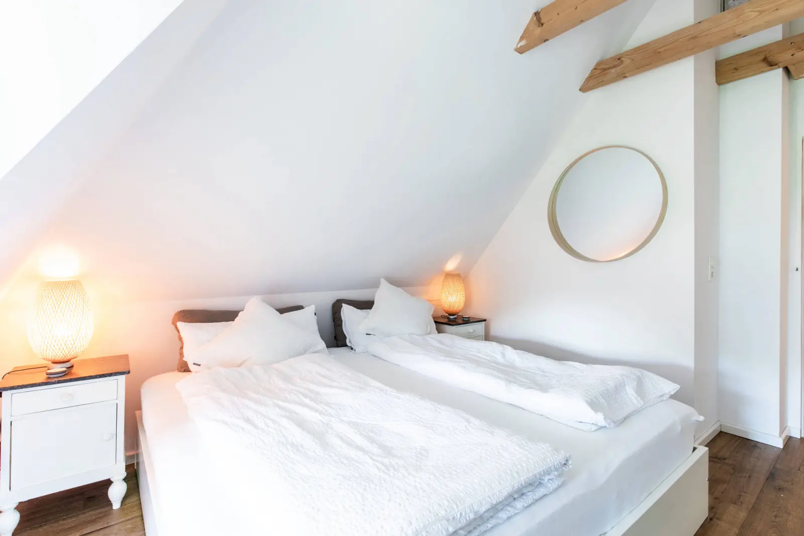 Schlafzimmer unterm Dach mit Doppelbett, weißer Bettwäsche und Rundspiegel