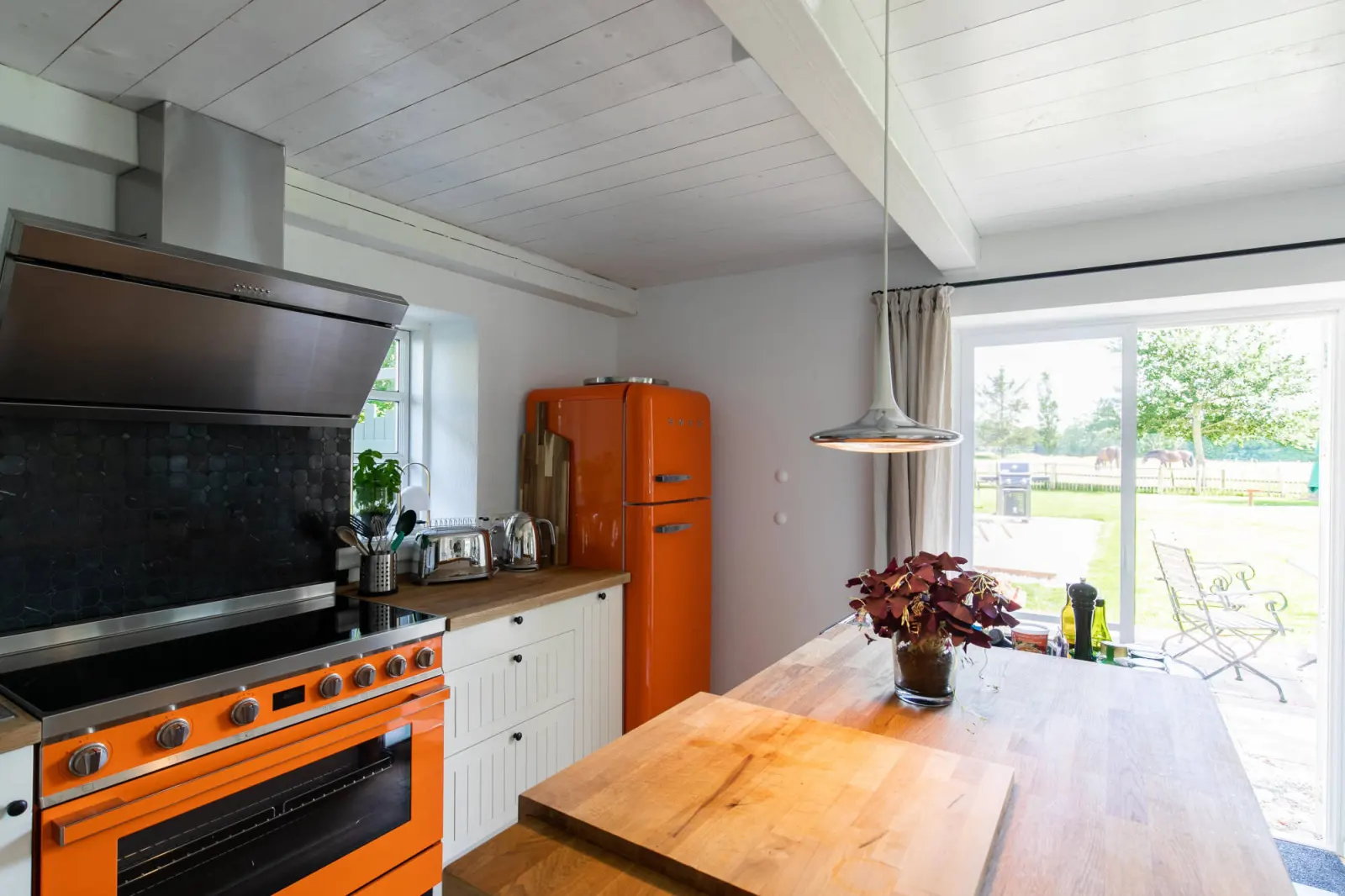 Küche mit orangem Herd und Kühlschrank, Holzarbeitsplatte und Terrassentür