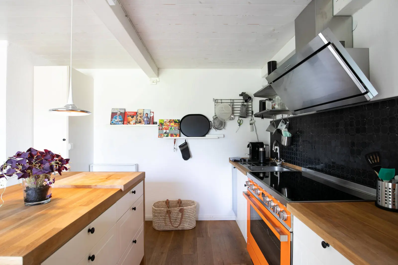 Küchenzeile mit Dunstabzug, Holzinsel und Pflanze unter weißer Holzdecke