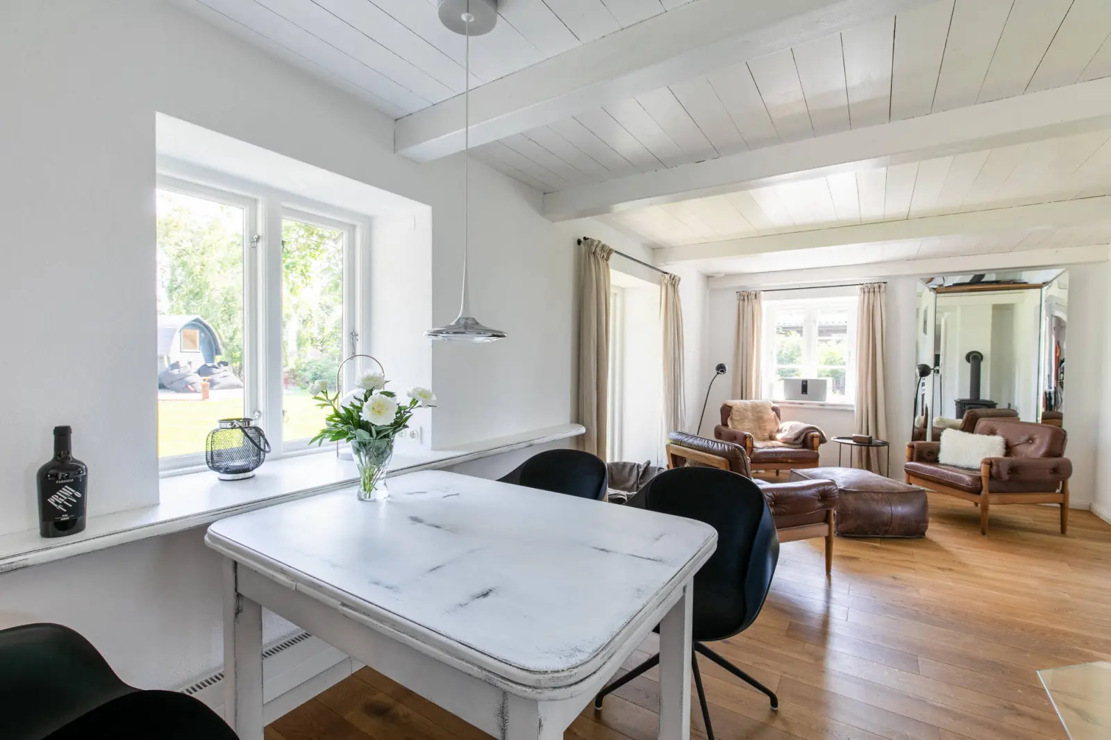 Weißer Esstisch mit Blumenstrauß und Blick zur Sitzgruppe im Wohnraum