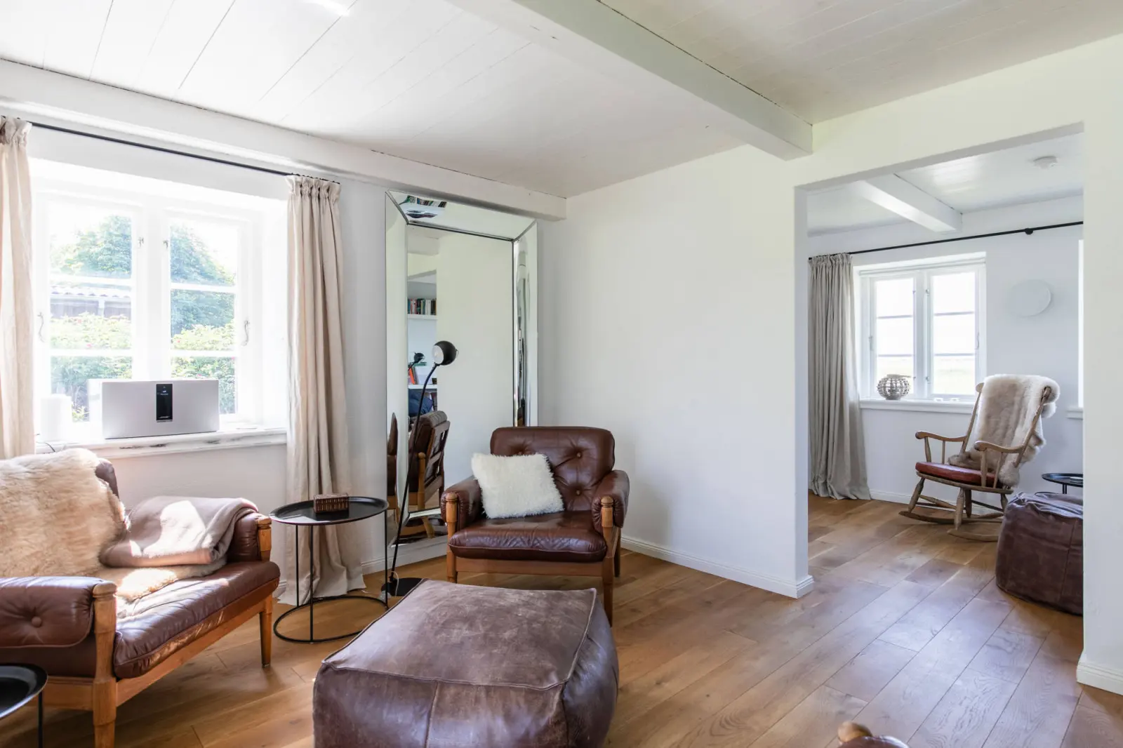 Wohnzimmer mit Ledersofa, Pouf, Spiegel und Schaukelstuhl im Hintergrund
