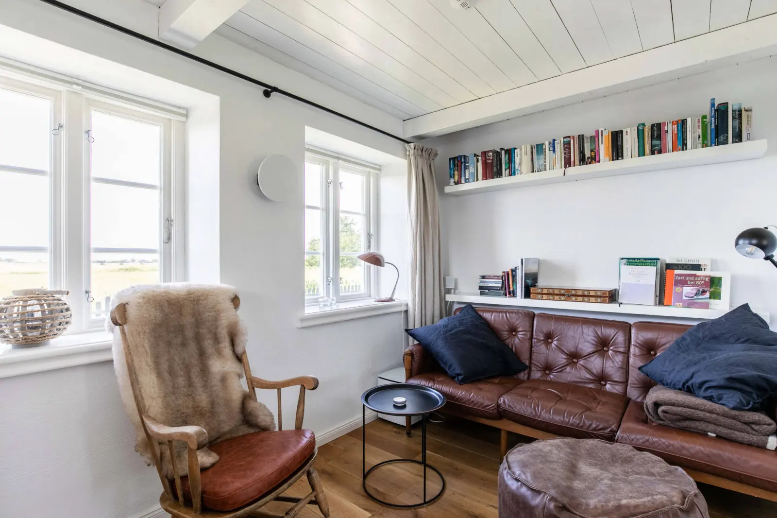 Schaukelstuhl und braunes Ledersofa mit Bücherbord darüber