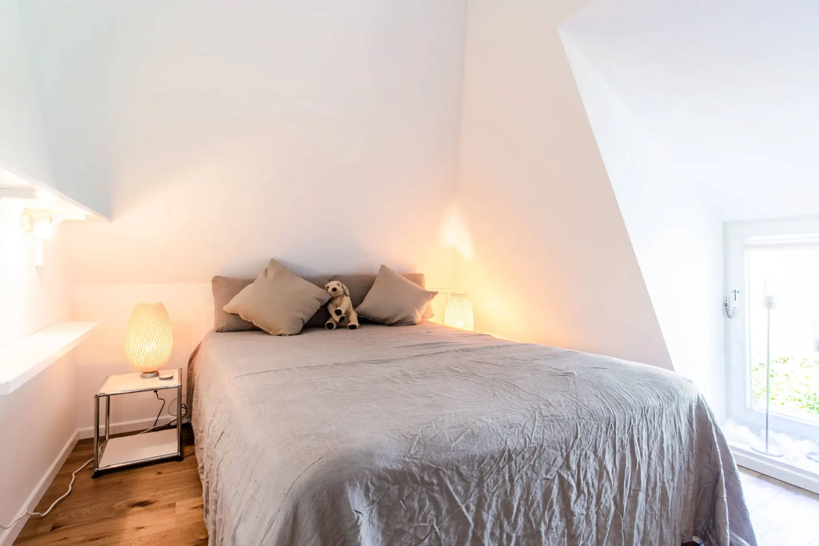 Bett mit grauer Tagesdecke und Kissen unter der Dachschräge