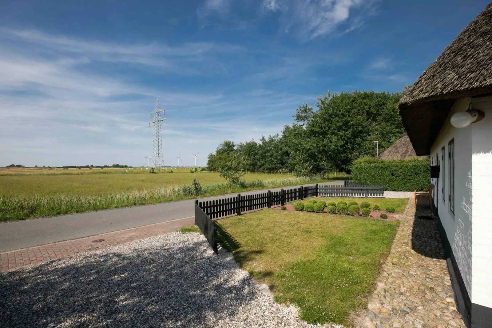 Straße und Marschlandschaft neben dem weiß gestrichenen Reetdachhaus