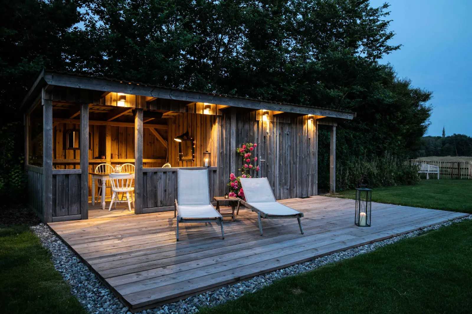 Beleuchteter Holzpavillon mit Sonnenliegen in der Abenddämmerung