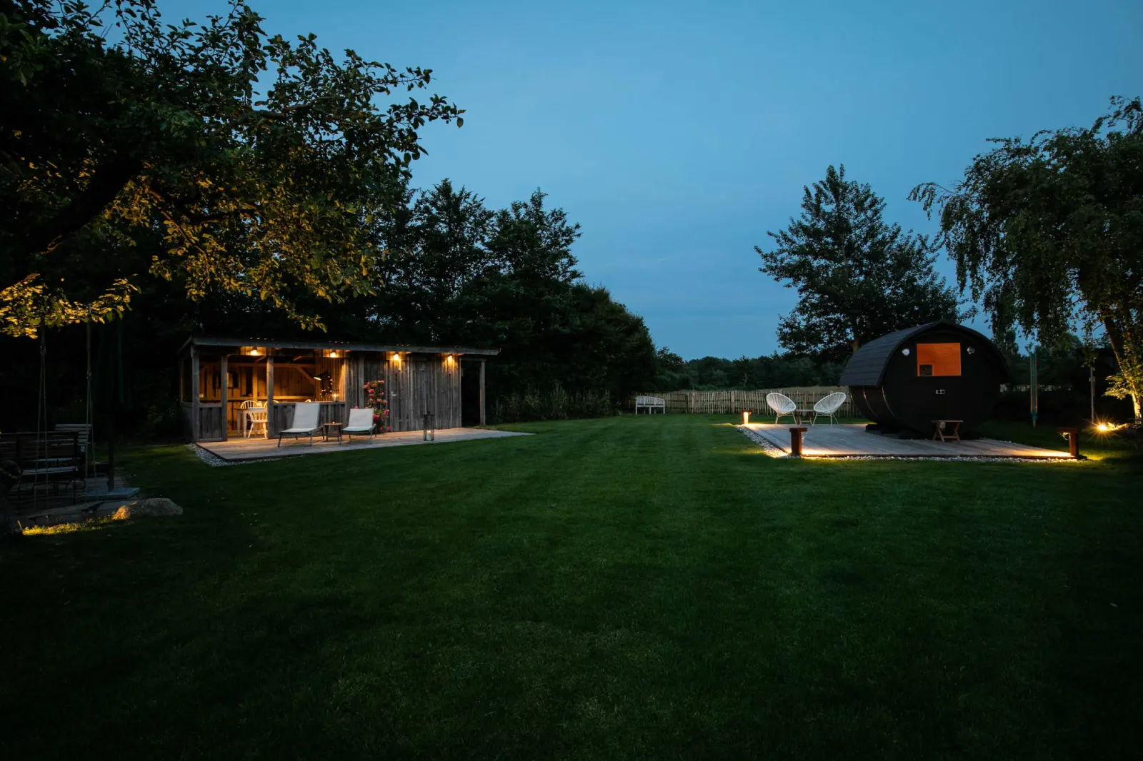 Abendlicher Garten mit Pavillon, Fasssauna und gedimmter Beleuchtung