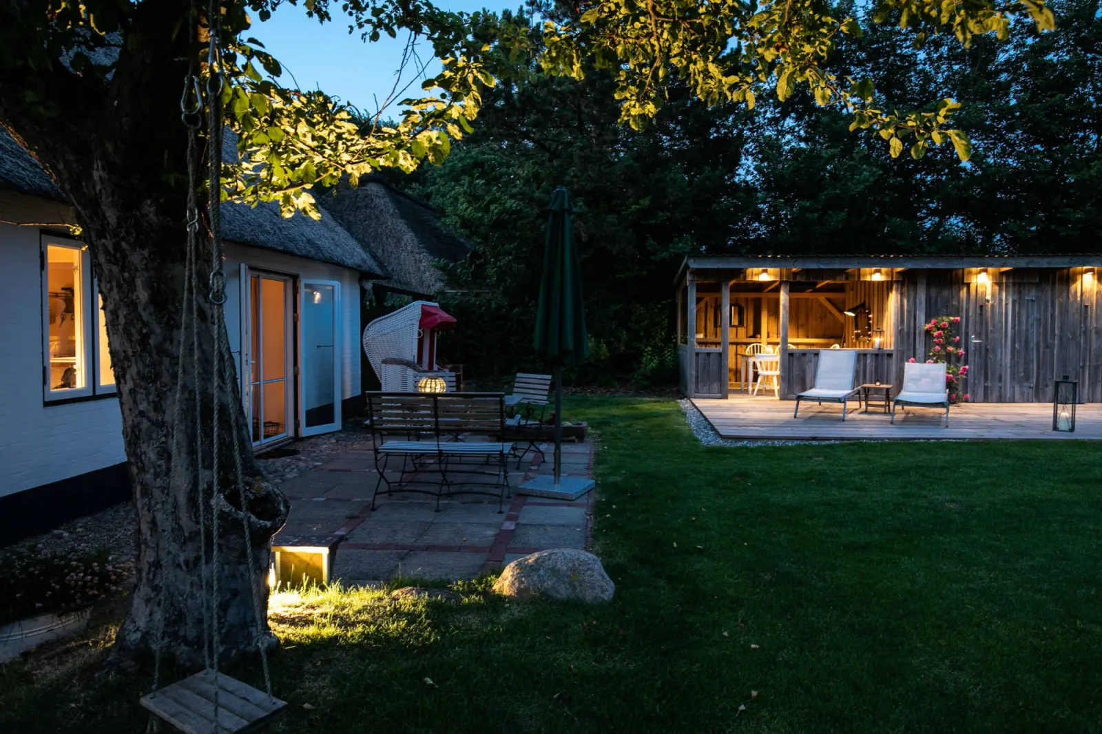 Terrasse unter dem Baum mit Schaukel und Blick zum beleuchteten Pavillon