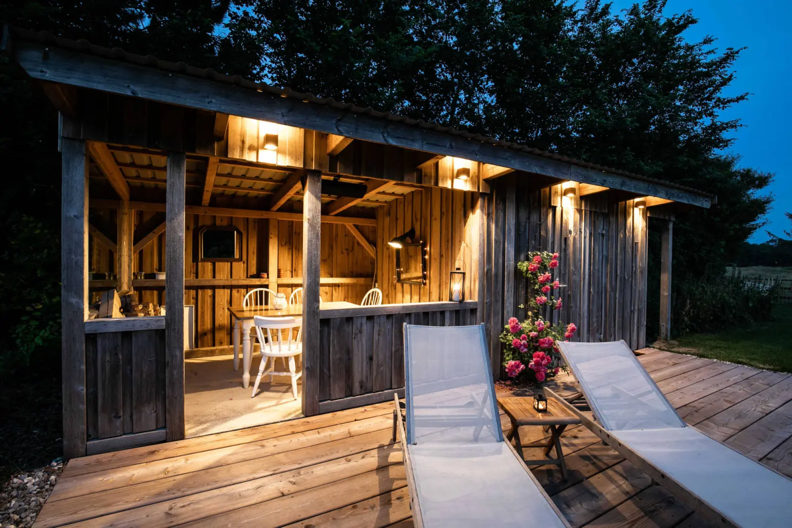 Pavillon mit Lichterkette, Sonnenliegen und rosa Rosen am Abend