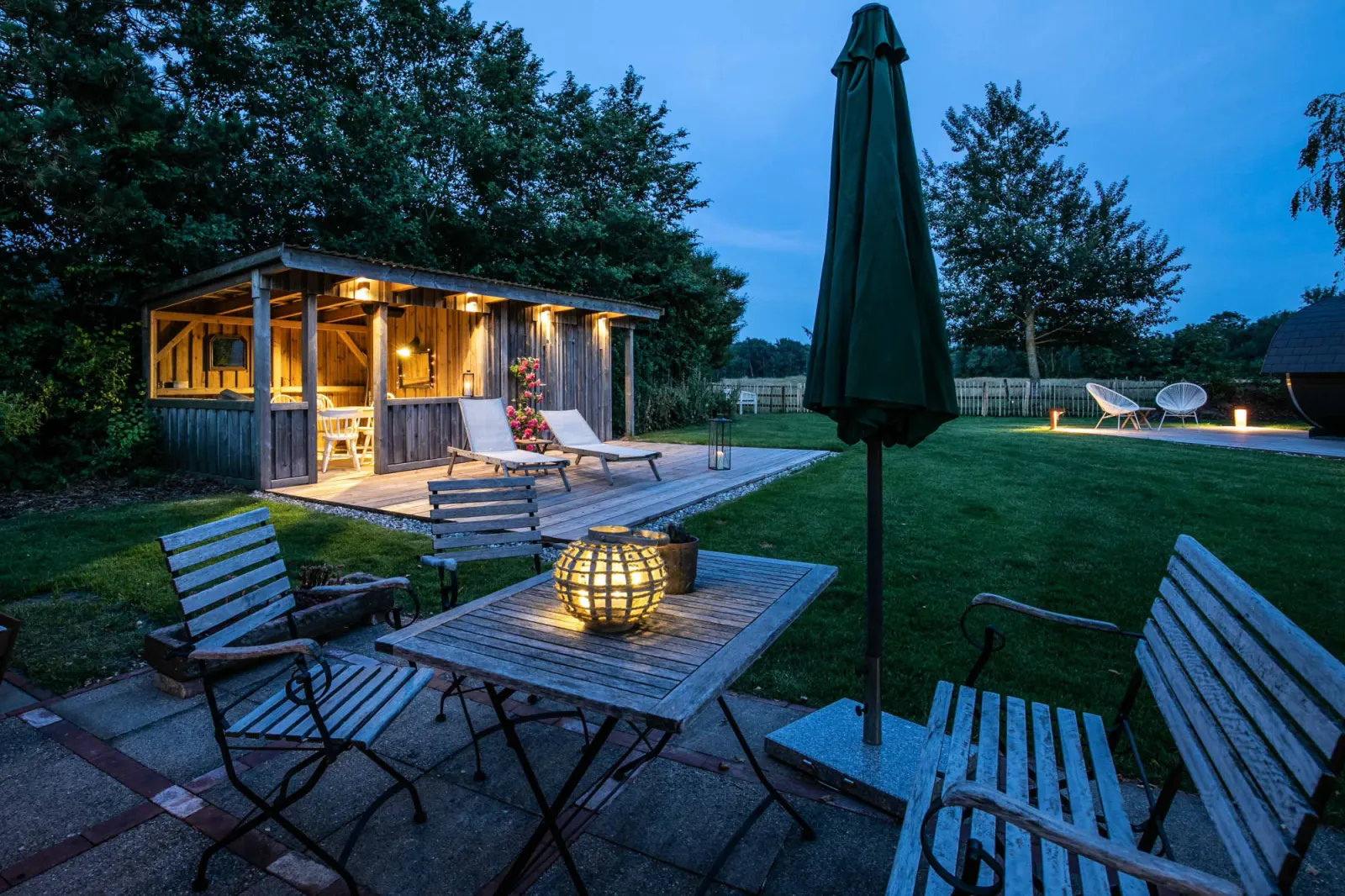 Sitzplatz mit Klappstühlen, Tisch und Windlicht, dahinter beleuchteter Pavillon