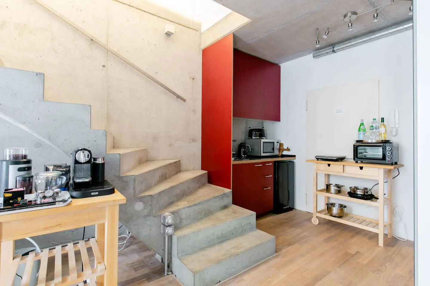 Kleine Küche unter der Betontreppe mit roten Schränken und Küchenwagen