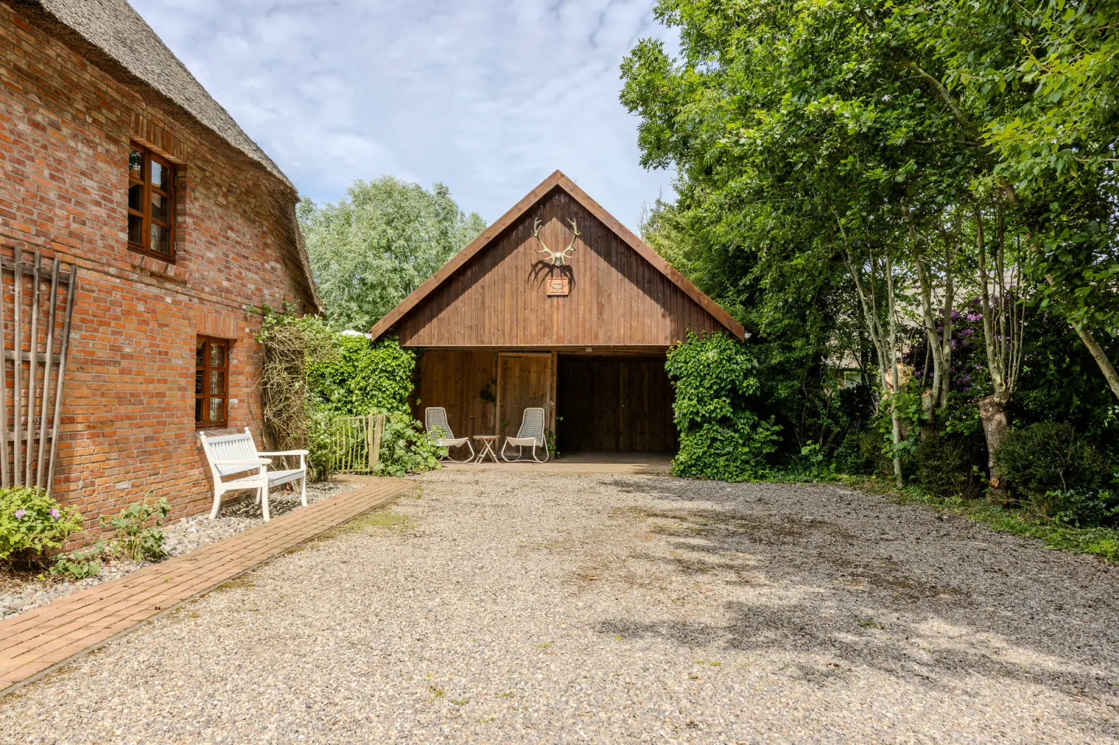 Kiesplatz vor dem Backsteinhaus mit offenem Holzcarport und Sitzbank
