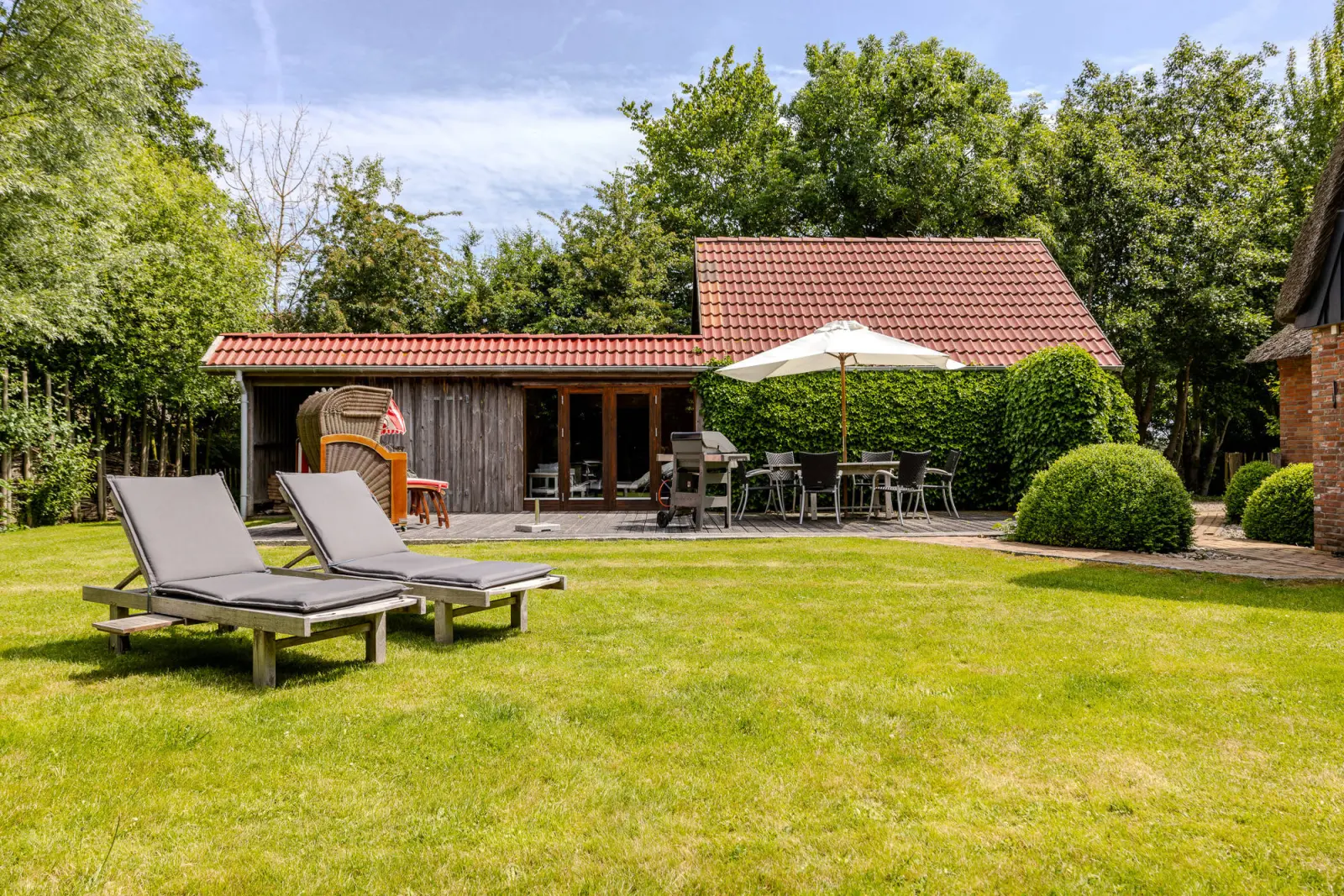 Gartenliegen auf dem Rasen, dahinter Terrasse mit Sonnenschirm und Nebengebäude