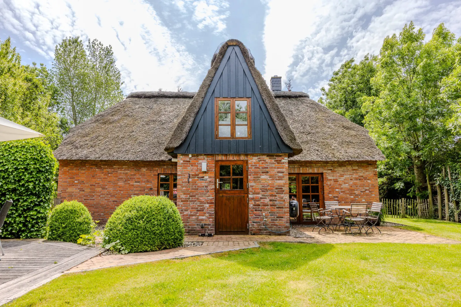 Hausgiebel mit blauer Holzverkleidung, Gartenrasen und Buchsbaumkugel im Sonnenlicht